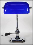 A vintage style bankers desk lamp having an adjustable blue glass shade raised on a chromed