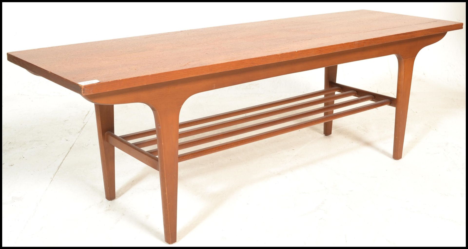 A mid century Danish influence teak wood long john coffee table being raised on tapering legs with a