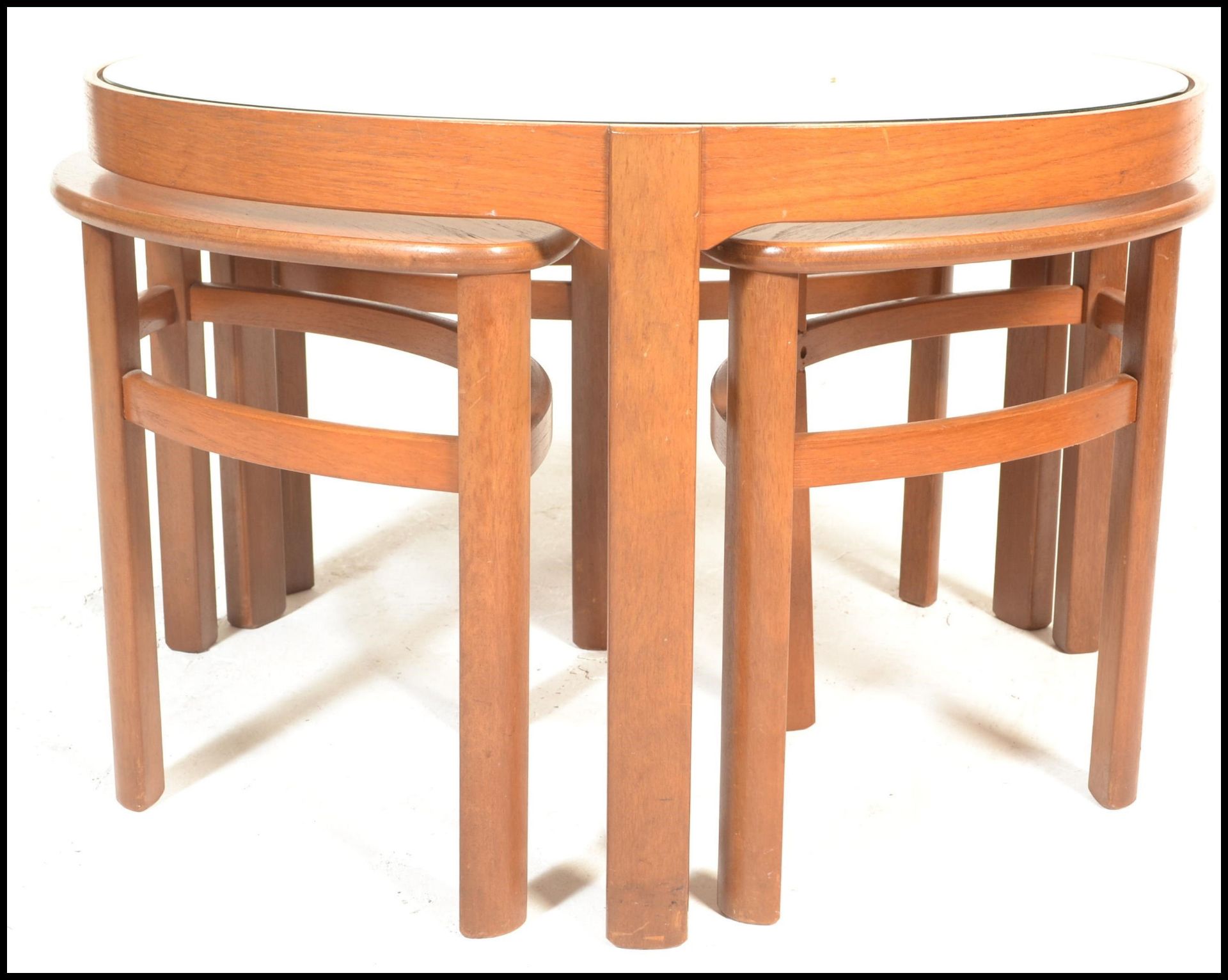 A retro 1970's Nathan teak and glass Trinity quartetto nest of table being raised on shaped legs