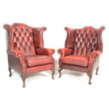 A pair of 20th Century Antique style red oxblood Chesterfield button back wing armchairs being