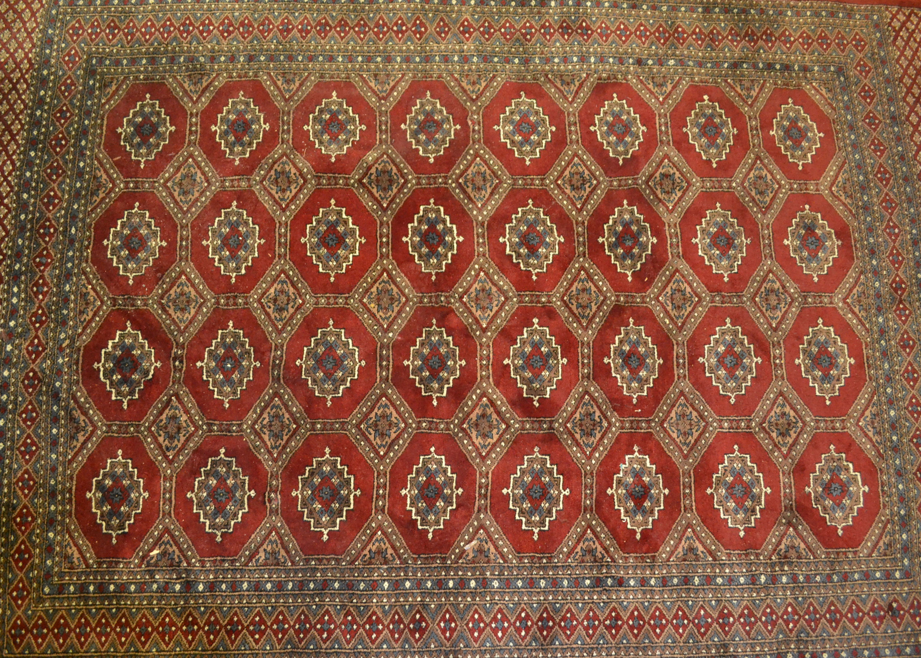 A 20th Century hand knotted floor rug carpet of large proportions in a Bukhara design having a red