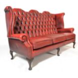 A 20th Century Antique style red oxblood leather chesterfield three seat sofa settee being raised on