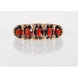 An English hallmarked 9ct yellow gold ring set with five graduating oval faceted cut red stones on a