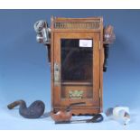 An early 20th Century oak smokers cabinet with single glazed door together with a selection of pipes