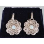 A pair of silver drop earrings of round knot form set with CZ's having central opal panels.
