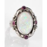 A 20th Century silver ring set with an oval opal panel and four red stones in a scrolled