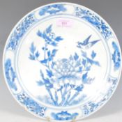 A 19th Century Chinese blue and white plate being hand painted with peonies and birds, the rim