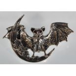 A silver brooch in the form of a bat standing on the moon with its wings open set with red stone