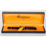 A boxed Waterman fountain having a dark red marble effect body with gold tone banding. The nib
