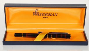 A boxed Waterman fountain having a dark red marble effect body with gold tone banding. The nib