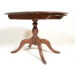 A 20th century Ercol beech and elm wood circular extending dining table being raised on a tripod