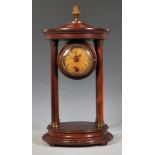 An early 20th Century mahogany portico mantel clock raised on a round plinth base, the round clock