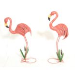 A pair of patterned pressed metal garden ornamental flamingos having a painted pink feathered finish