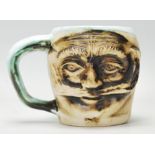 A Devon studio art pottery mug signed Andre Loret having a modelled male face to the front with a