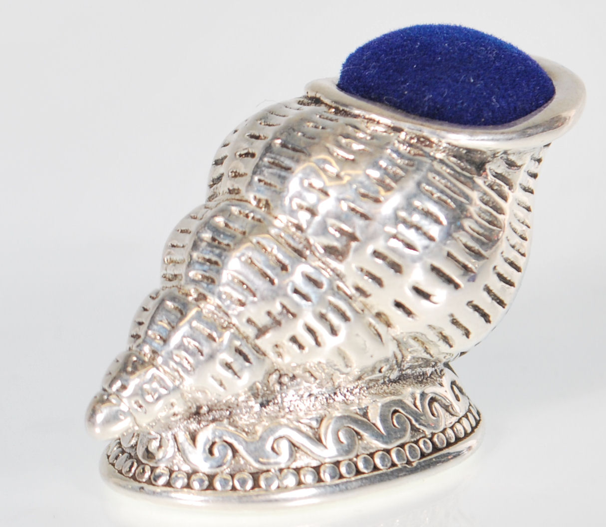 A stamped 925 silver pin cushion in the form of a conch shell raised on a footed base with a blue