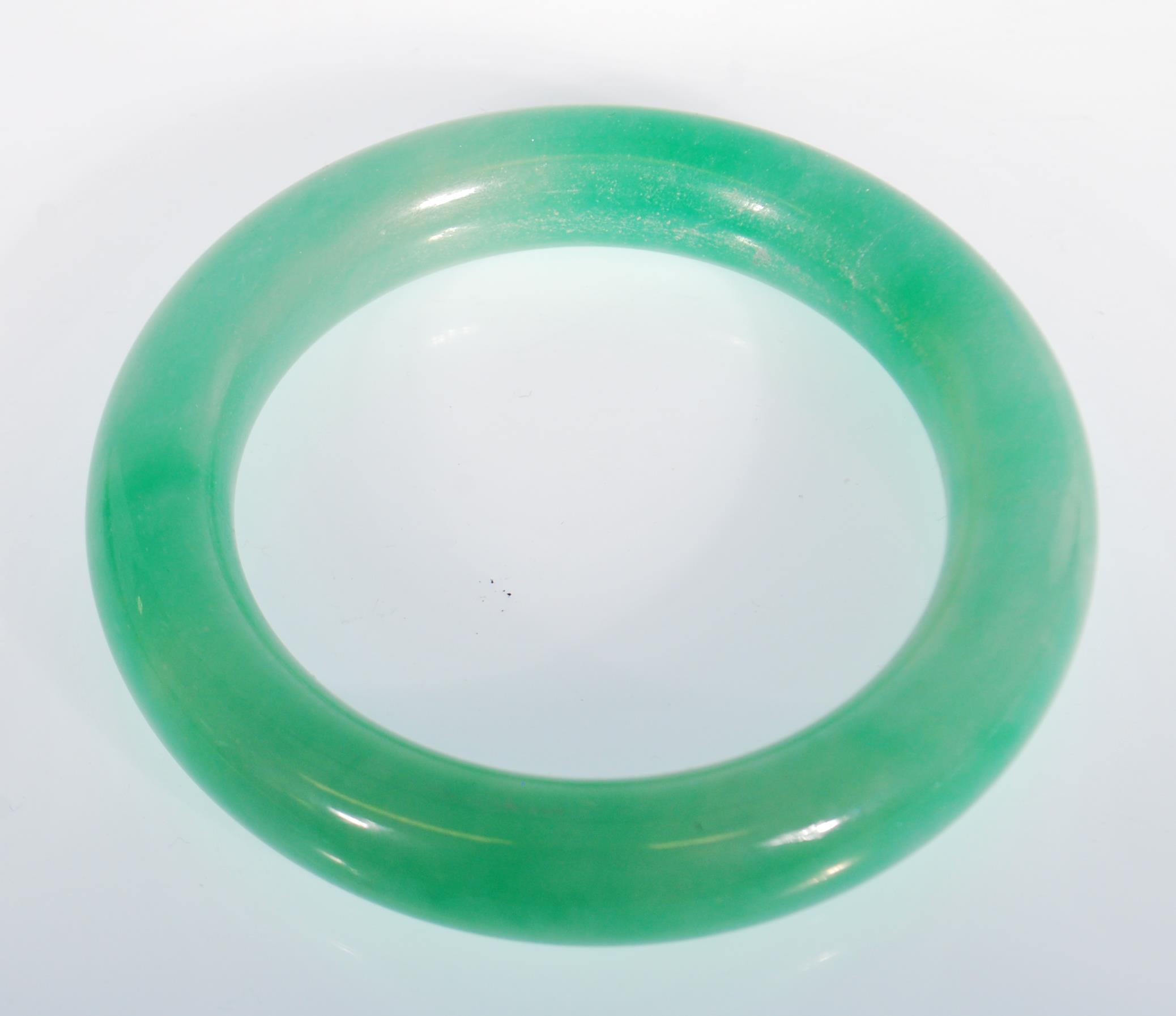 A Chinese green jade bangle of typical round form. Interior diameter 5.9g. Measures 99.4g.