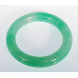 A Chinese green jade bangle of typical round form. Interior diameter 5.9g. Measures 99.4g.