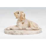 An early 20th century carved stone hound dog modelled recumbent on a ovular marble base, complete