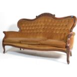 A Victorian style carved mahogany Rococo style sofa with shaped and carved cresting rail over a deep