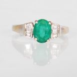 A hallmarked 18ct white gold ring set with an oval cut emerald with diamond accent stones to the