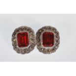 A pair of ladies silver stud earrings set with rectangular cut garnets having a halo of