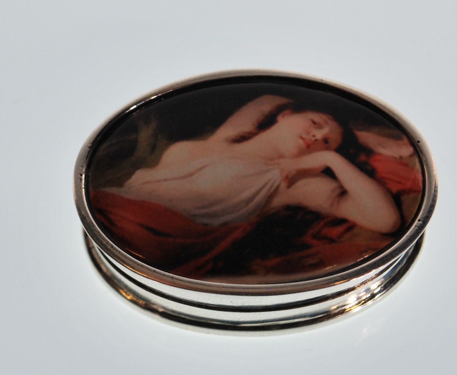 A stamped 925 silver pill pot of oval form having an enamelled lid depicting a classical female