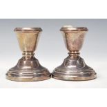 A pair of silver hallmarked stub candlesticks raised on terraced bases having single sconces.