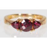 A 9ct gold (stamped 9k) Rhodolite garnet three stone dress ring, the ring set with central faceted