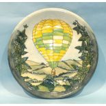 A Moorcroft charger decorated with a yellow, green and white hot air balloon in a landscape,