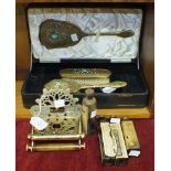 A three-piece gilt metal decorated cased dressing table set, comprising of hair brush, clothes brush