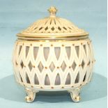 A Belleek porcelain reticulated bowl and cover, with floral finial and standing on four scroll feet,