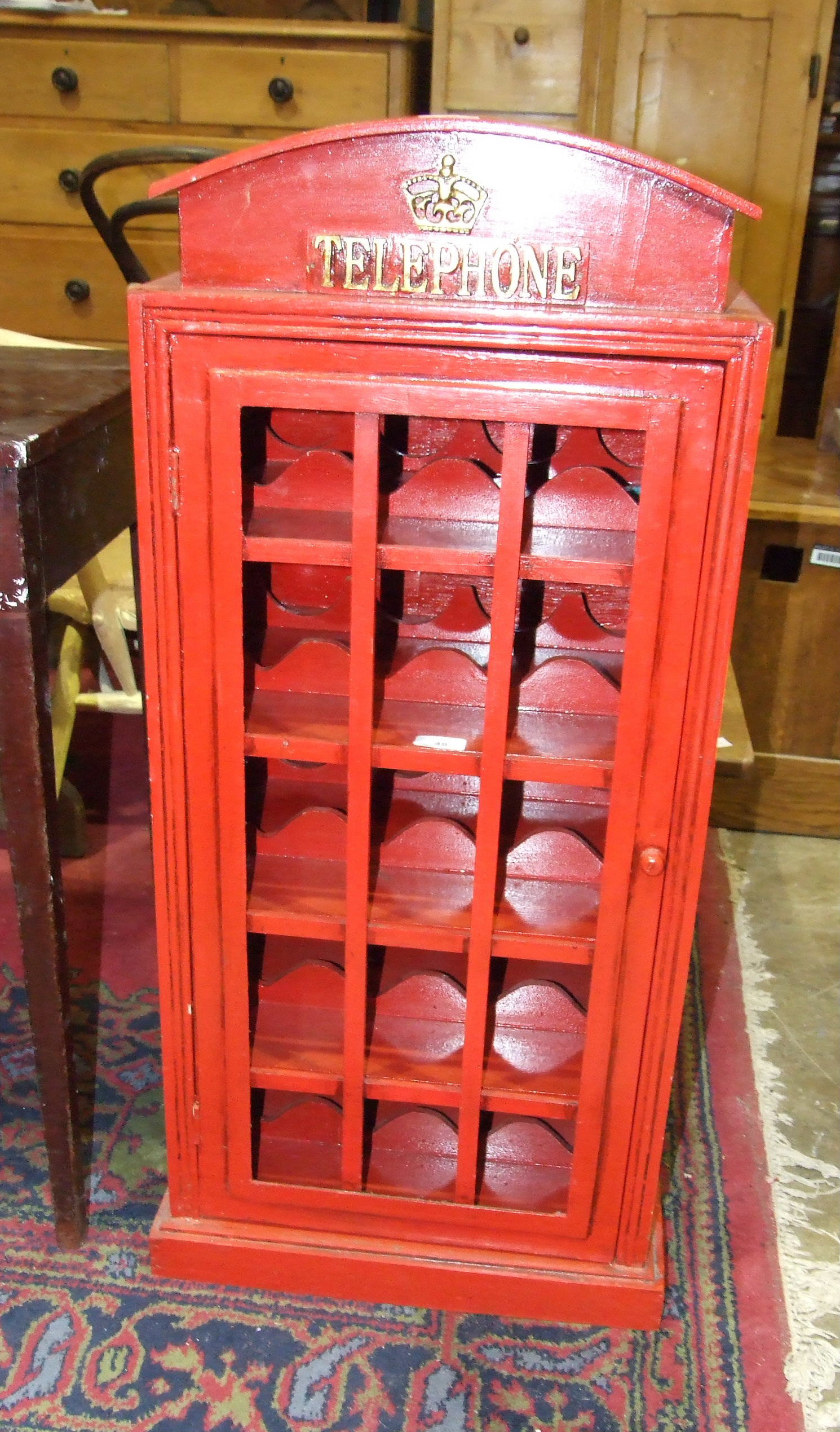 A red painted wine rack in the form of a telephone box, fitted with a glazed door and four bottle