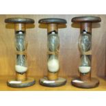 Three large wood and glass egg timers with circular tops and bases, each 23cm high, (3).