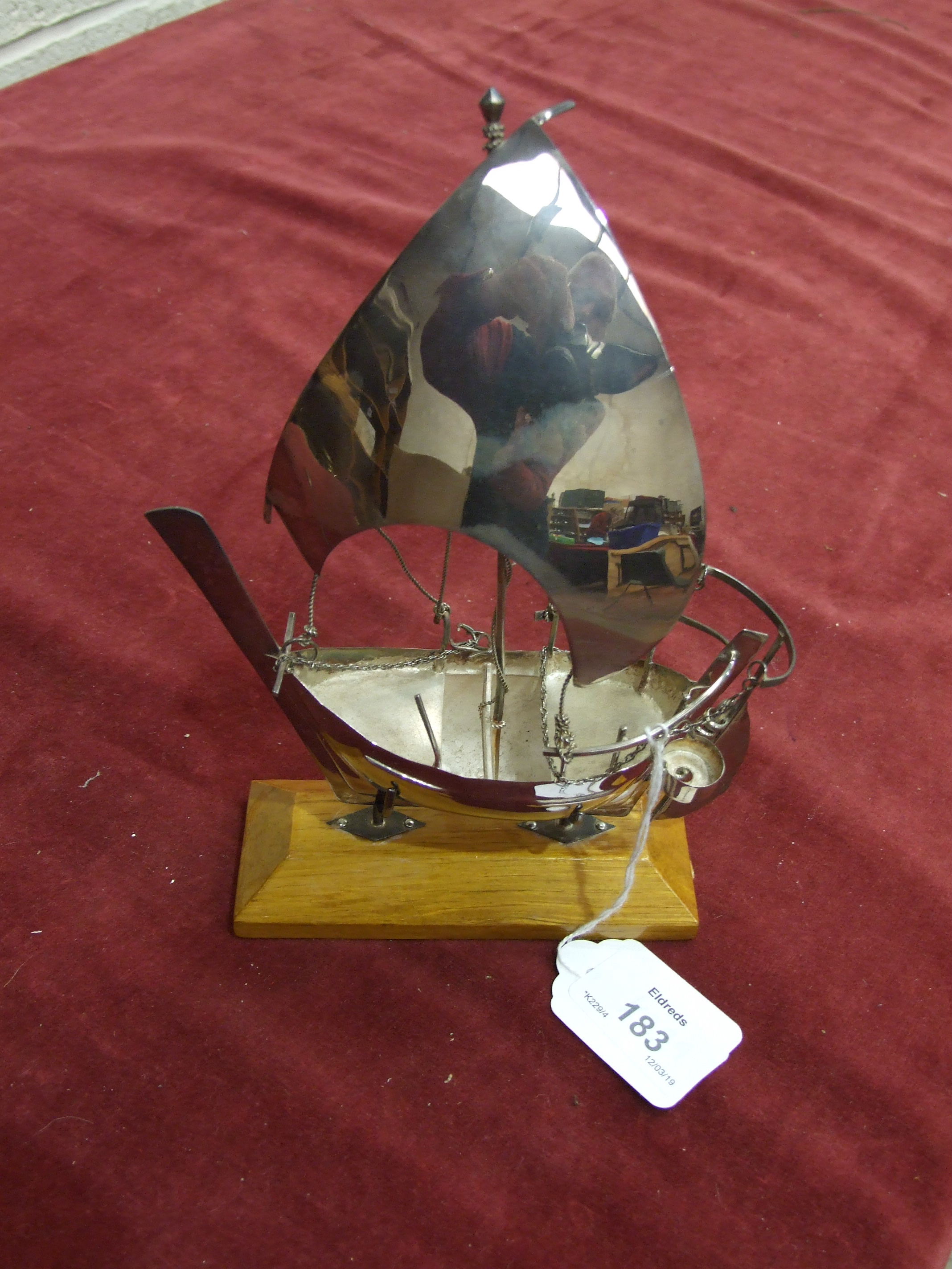 A white metal model of a dhow, on wood stand, 18cm high, in fitted box.