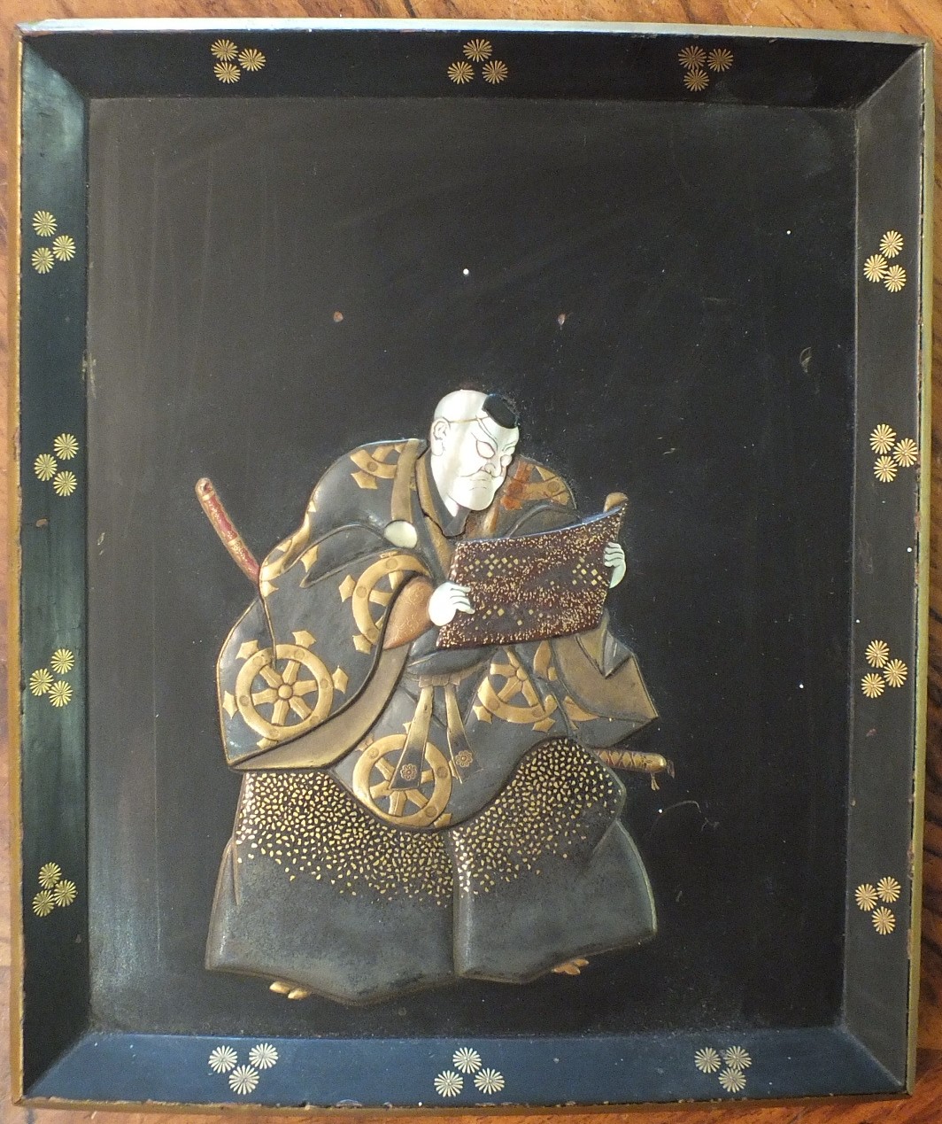 An early 20th century lacquered wood shallow tray decorated in relief with a Samurai reading from