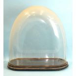 A large clock glass dome of oblong form with rounded ends on turned wood base, 61cm high.