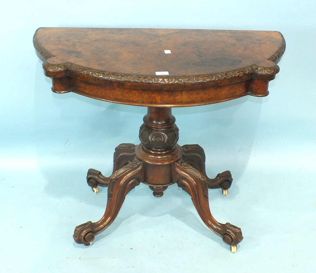 A Victorian walnut fold-over card table, the shaped top with carved border, on turned and carved