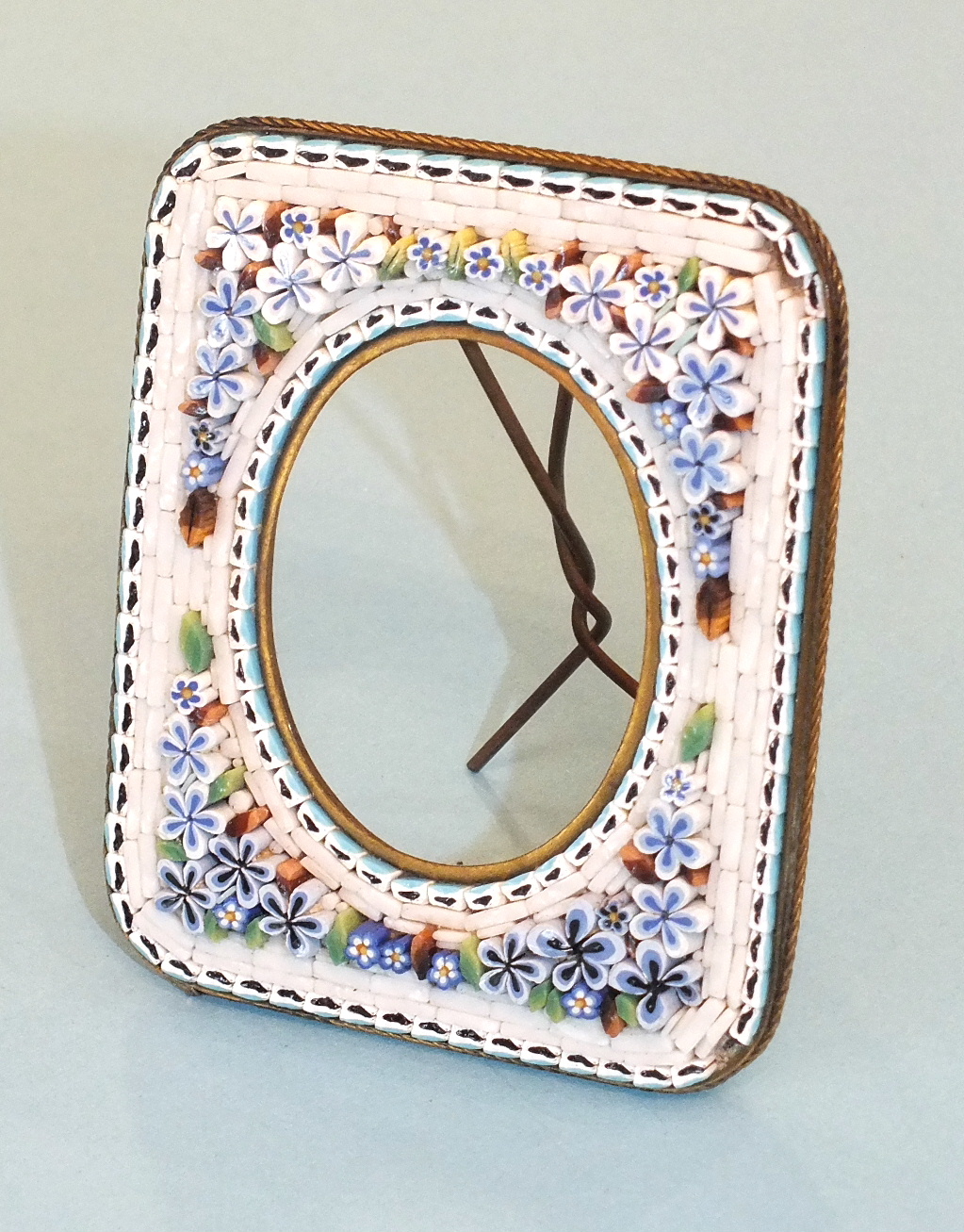 A miniature glass mosaic picture frame decorated with blue and white flowers around an oval