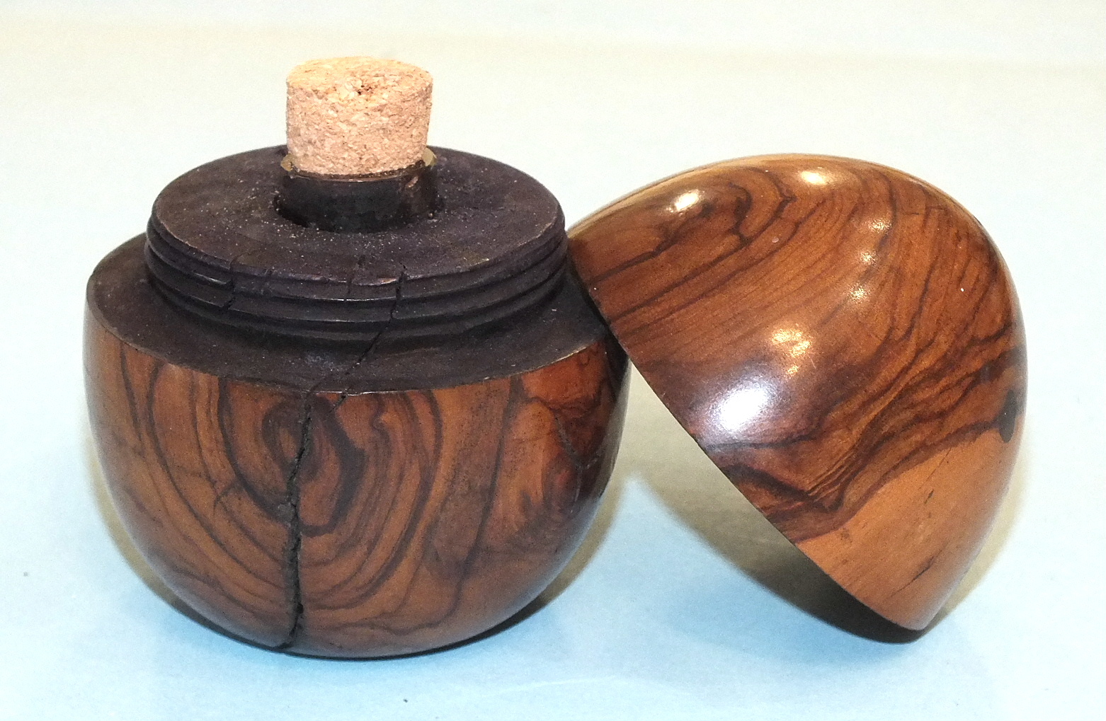 An olive wood egg-shaped travelling inkwell, the screw top over a glass bottle, 6.5cm high.