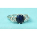 A sapphire and diamond ring claw-set an oval sapphire between two brilliant-cut diamonds, in