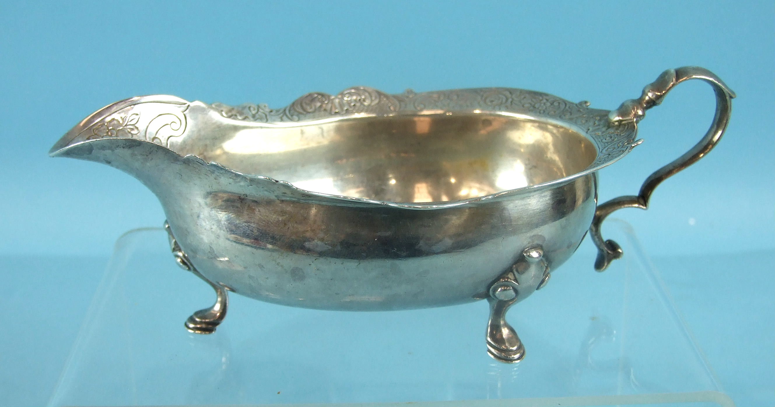 A George II Scottish cream or sauce boat on three hoof feet, with a shaped and chased rim and scroll