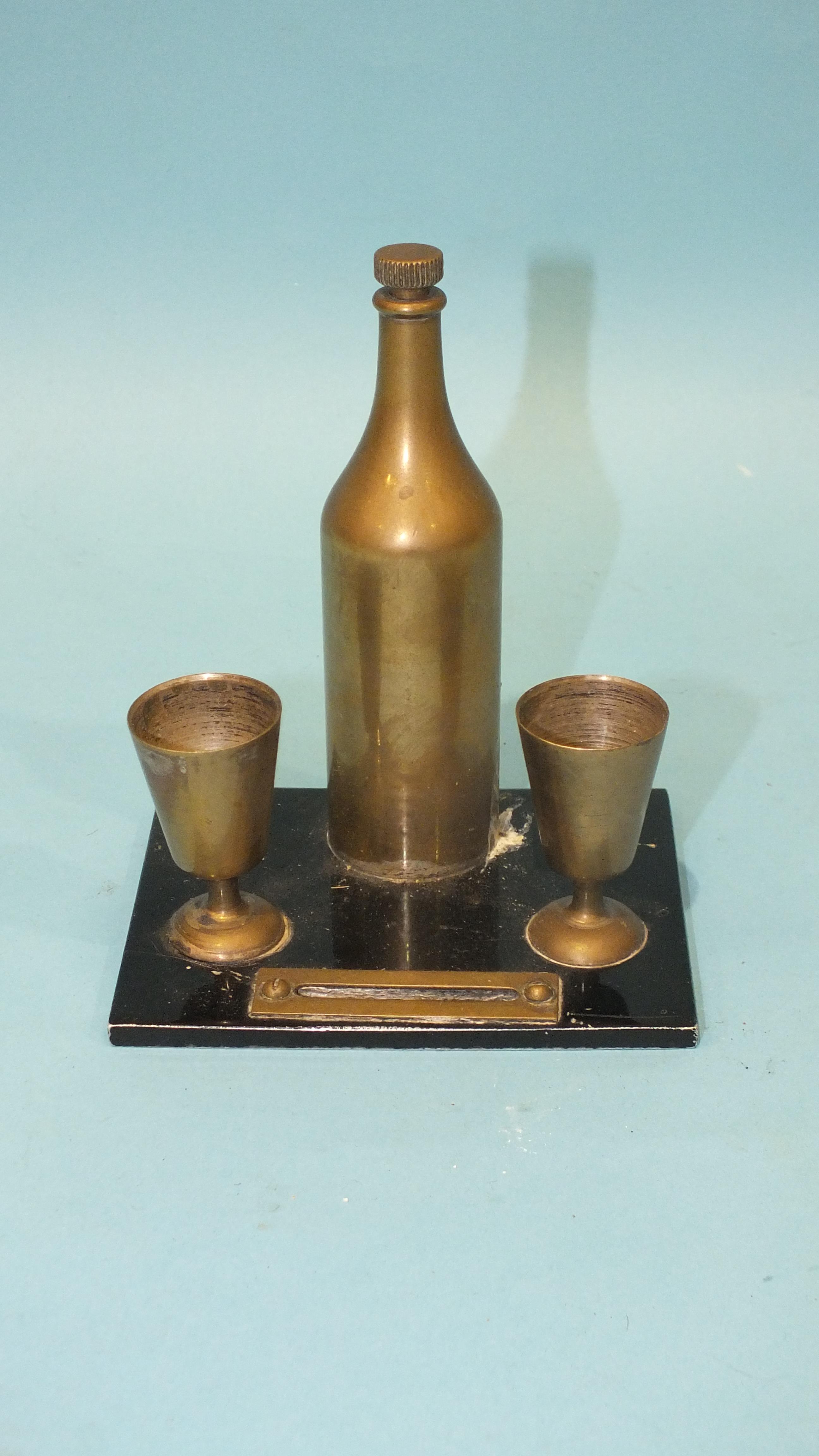 A small table match strike in the form of a brass bottle and two goblets, the bottle top pulling out