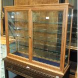 A modern display cabinet with grained wood frame, glass back and sides and a pair of glazed doors,