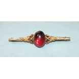 A gold bar brooch set garnet cabochon, (tested as 18ct gold approximately), metal pin, 5.8g.