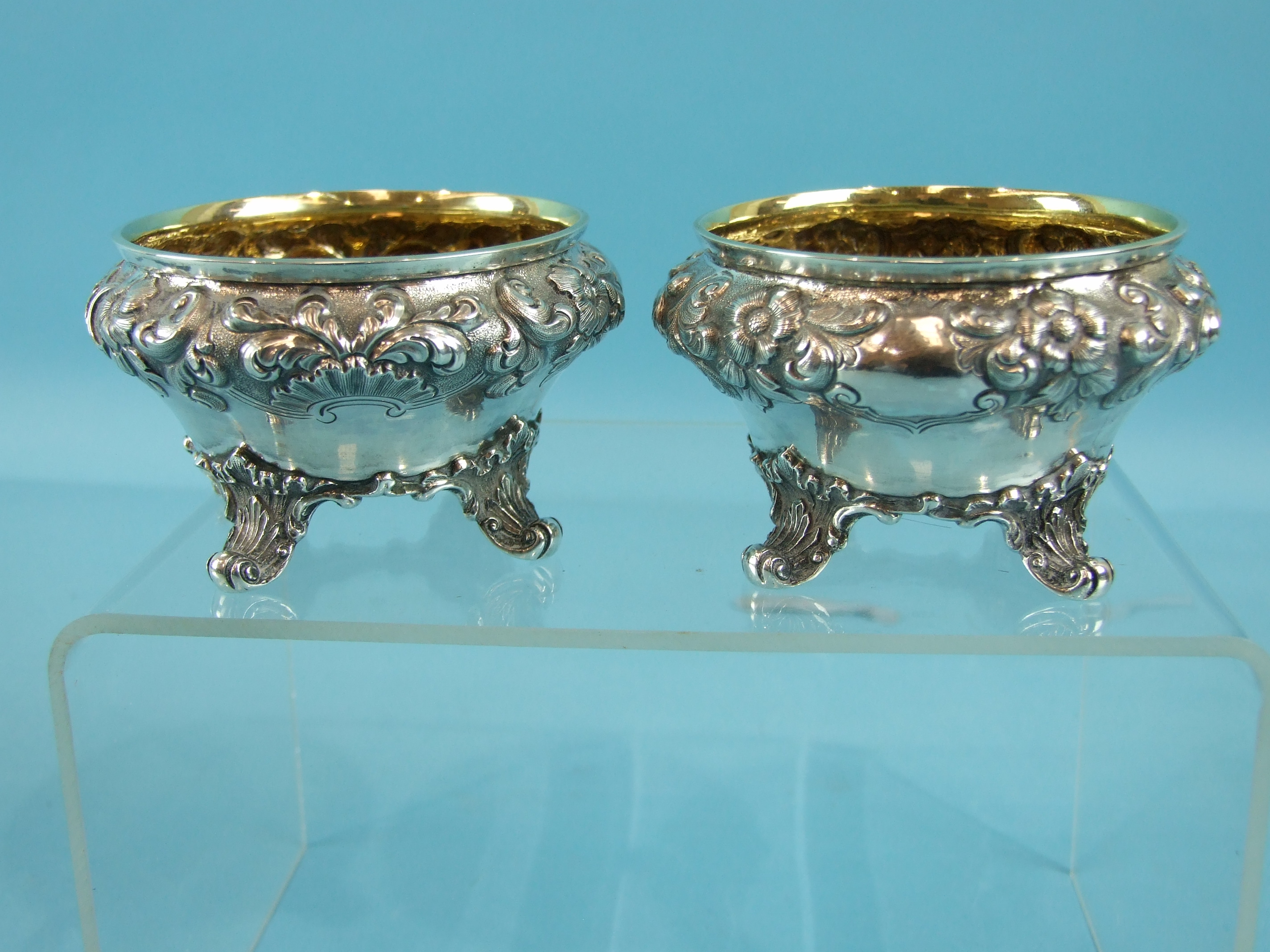 A pair of Victorian salts of compressed circular form embossed with flowers and foliage, on four