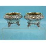 A pair of Victorian salts of compressed circular form embossed with flowers and foliage, on four