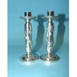 A pair of Chinese white metal candlesticks with raised dragon decoration, on circular bases,