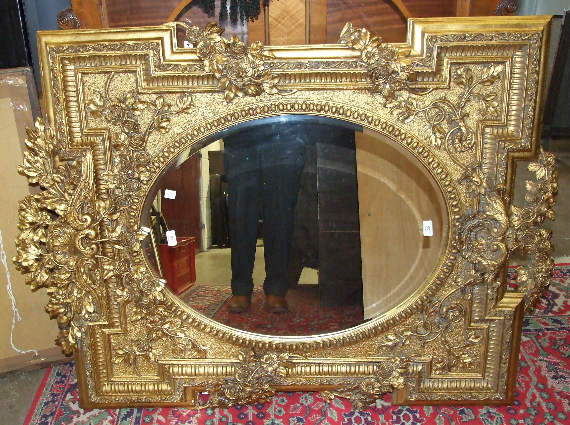 A large gilt-framed wall mirror, the bevelled oval plate within shaped frame heavily-moulded with