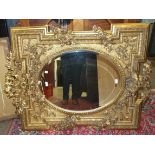 A large gilt-framed wall mirror, the bevelled oval plate within shaped frame heavily-moulded with
