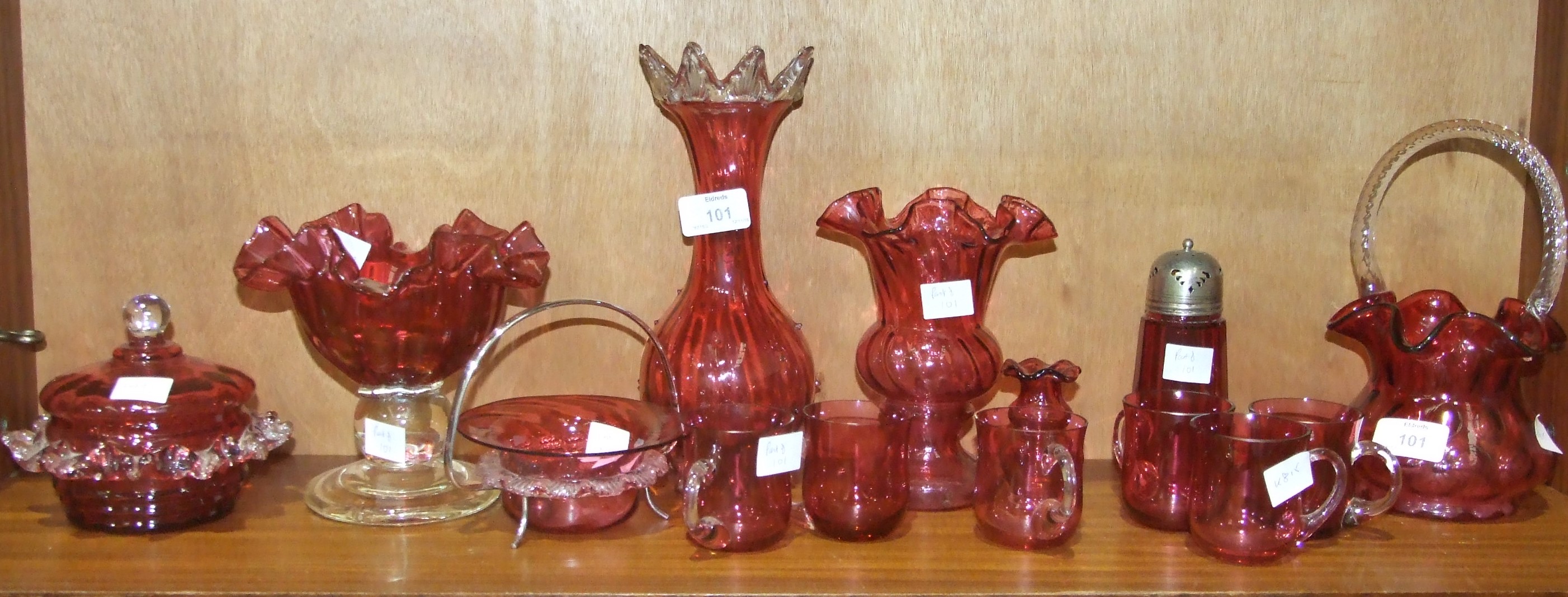 A collection of cranberry glassware, including a basket with frilled rim and white glass handle,